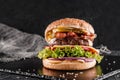 Beef burger with lettuce, tomatoes, slice of cheese, ham, pastrami and sauce on slate black background, close up Royalty Free Stock Photo