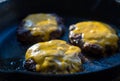 Beef burgers on frying pan with melting cheddar cheese