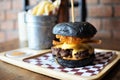 Beef cheese burger in charcoal bun on wooden plate. Royalty Free Stock Photo