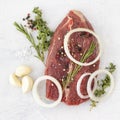 Beef, garlic, onion, mixed pepper, salt, thyme, rosemary. Raw, fresh beef meat with spices on a white stone background Royalty Free Stock Photo