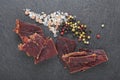 Beef jerky with peppercorns and salt on black stone table. Top view Royalty Free Stock Photo