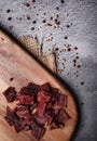 Beef jerky on wooden cutting board, on dark stone countertop, vertical view. Dried beef meat chips.