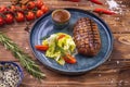 Beef patty on a platter with vegetables, lettuce, bell pepper, rosemary, garlic and sesame seeds on a brown wooden background Royalty Free Stock Photo