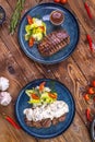 Beef patty on a platter with vegetables, lettuce, bell pepper, rosemary, garlic and sesame seeds on a brown wooden background Royalty Free Stock Photo