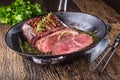 Beef steak. Juicy medium Rib Eye steak slices in pan on wooden board with fork and knife herbs spices and salt Royalty Free Stock Photo