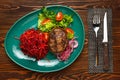 Beef steak with a side dish of carrots, beets and tomatoes on a green plate