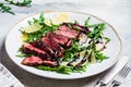 Beef steak tagliata with arugula and parmesan on gray plate, gray background. Italian cuisine concept