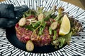 Beef steak tartare with capers on an unusual ceramic plate. Main course appetizer. Close up, selective focus