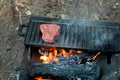 Beef steaks grilling on a cast iron plate on a camp fire. Campfire cooking. Royalty Free Stock Photo