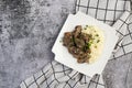 Beef stroganoff with mashed potatoes and herbs on a white square plate on a dark background Royalty Free Stock Photo