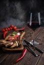 Beef Tartar with a raw egg yolk, a glass of red wine, rye bread and chilis on a wooden board with spoon and fork. Smoke background Royalty Free Stock Photo