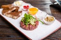 Beef tartare with arugula salad, crisp bread chips, sauces and snacks on white plate on the served restaurant table