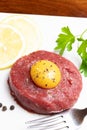 Beef tartare with egg yolk on a wooden table and white plate