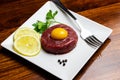 Beef tartare with egg yolk on a wooden table and white plate