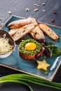 Beef tartare served with an egg yolk, chopped green onions, toast and butter in plate on dark stone background. Clean eating Royalty Free Stock Photo