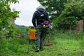 The beekeeper in a protective working suit mows tall grass with hands petrol trimmer around the bee hives on a summer day in the Royalty Free Stock Photo