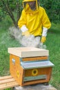 A beekeeper uses a smoker over the hive to calm bees before raising the frames