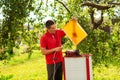 Beekeeper in red t-shirt cuts wax from honeycomb frame with a special electrik knife near the honey extractor