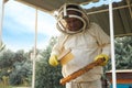 Beekeeper in uniform brushing honey frame at apiary