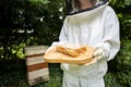 Female Beekeper In Protective Clothing Outside Honey Bee Hive Holding Honeycomb Royalty Free Stock Photo