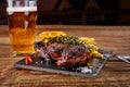 Beer being poured into glass with gourmet steak and french fries on wooden background. Royalty Free Stock Photo