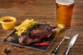 Beer being poured into glass with gourmet steak and french fries on wooden background. Royalty Free Stock Photo