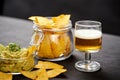 Beer and a bowl of guacamole with nachos on an old black wooden table Royalty Free Stock Photo