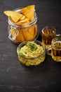 Beer and a bowl of guacamole with nachos on an old black wooden table Royalty Free Stock Photo