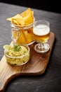 Beer and a bowl of guacamole with nachos on an old black wooden table Royalty Free Stock Photo