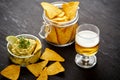 Beer and a bowl of guacamole with nachos on an old black wooden table Royalty Free Stock Photo