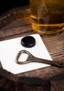Beer coaster with bottle top and opener and glass of beer on top of wooden barrel.