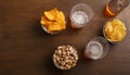 Beer festival. Two glasses of beer, bottle, pistachio, chips and nachos in plates on wooden brown table