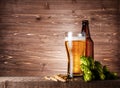 Beer in glass glass with bottle, hop cones and wheat on wooden brown background Royalty Free Stock Photo