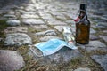 Beer and liquor bottles and a surgical face mask left on a cobblestone road, while bars have closed due to infection with