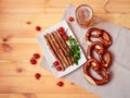 Beer mug, soft pretzels and plate with roasted sausages, cherry tomatoes and parsley on wooden table. Royalty Free Stock Photo