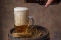 Beer mug with wheat ears on a wooden barrel and a dark background wall, pour beer from a bottle Royalty Free Stock Photo