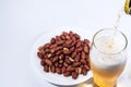 Beer is poured into a glass and peanuts in the saucer.