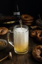 Beer pouring in glass with pretzels, bratwurst and snacks on rustic wooden table