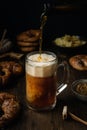 Beer pouring in glass with pretzels, bratwurst and snacks on rustic wooden table