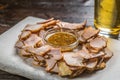 Beer snack of thinly sliced pieces of meat with a sauce of grainy mustard on the Board for filing is covered with a sheet of parch