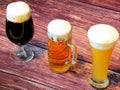 Beer, wheat, light and dark, in different glasses, stand in a row on a dark wooden table Royalty Free Stock Photo