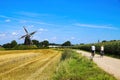 View on cycling track with cyclists in rural dutch maas landscape with windmill Molen de grauwe beer against blue summer sky