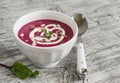 Beet soup in a white bowl on bright wooden surface