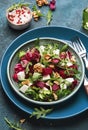 Beet summer salad with arugula, radicchio, soft cheese and walnuts on plate with fork, dressing and spices on blue kitchen table,