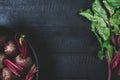 Beets with green tops in round metal pan on dark black wooden background, fresh red beetroot on backdrop kitchen table top view Royalty Free Stock Photo