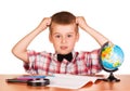 Befuddled boy sitting at table on notebook, pencils, globe .