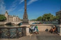 Beggar on bridge over the Seine River with sunny blue sky in Paris.