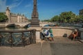 Beggar on bridge over the Seine River with sunny blue sky in Paris.