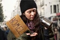 A beggar woman holds a cardboard sign with the inscription homeless and looks at coins from a steel begging cup Royalty Free Stock Photo