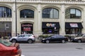 Beggars Pizza with black awnings and neon signs in the window, people standing on the sidewalk and cars on the street in downtown